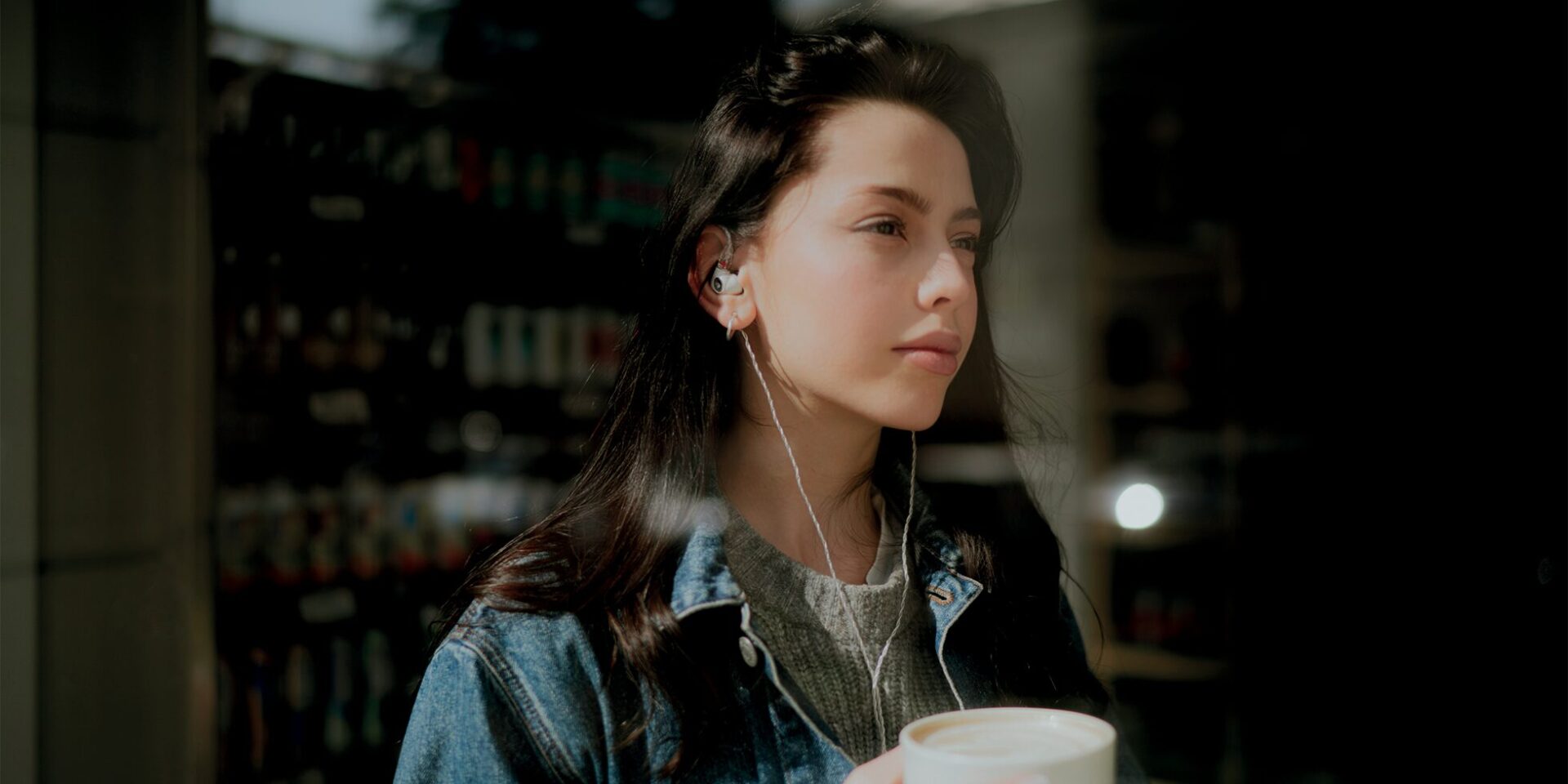 young woman wearing meze alba hifi earplugs holding a cup of coffee
